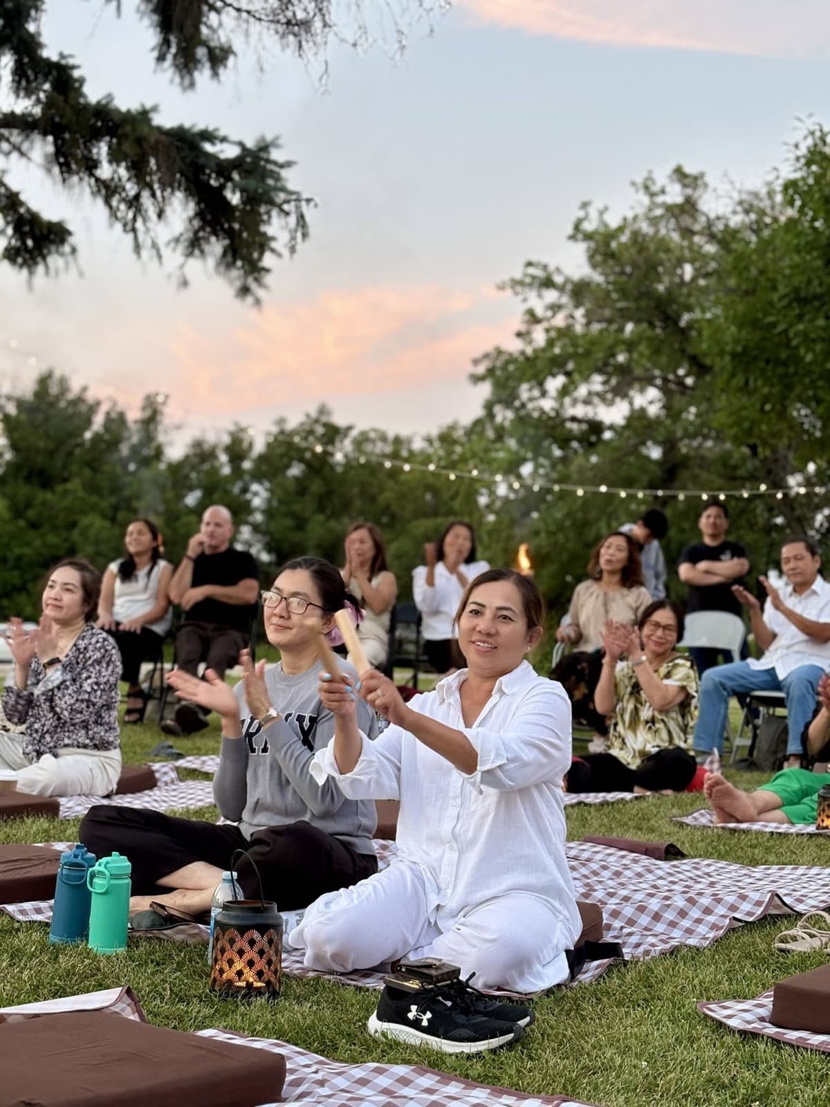 Listeners sitting on blankets, applauding under an evening sky.
