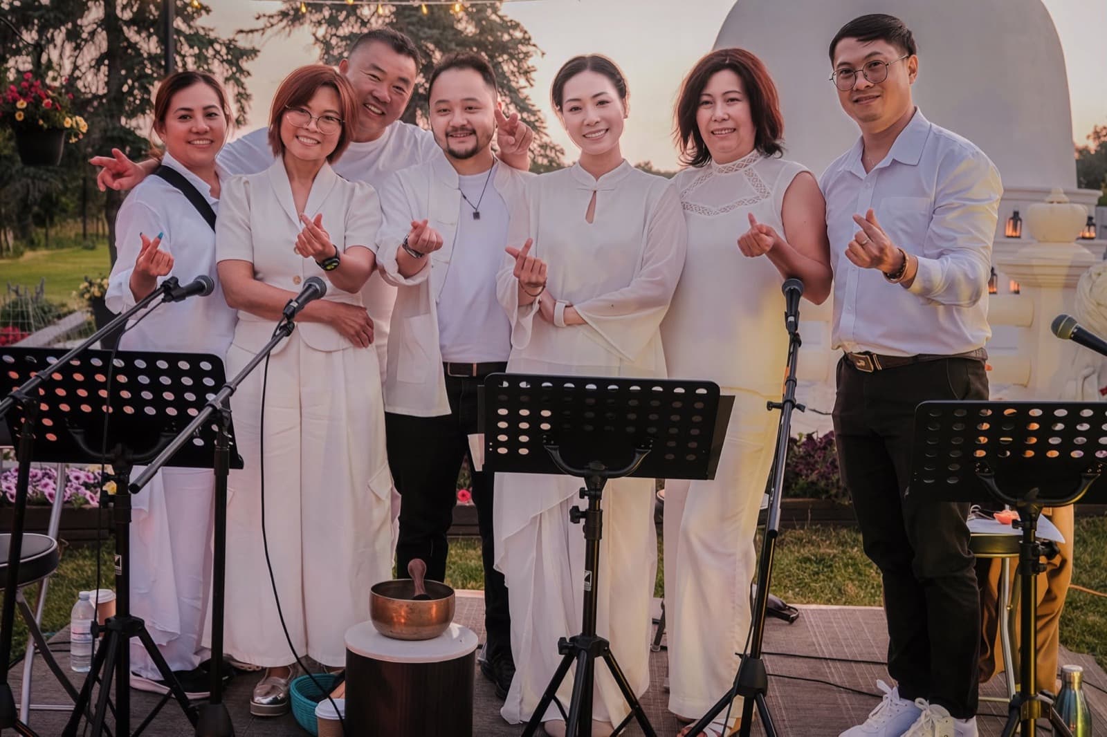 Singers in white making finger hearts beside the singing bowl.